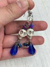 Load image into Gallery viewer, Mini Howlite Skull Bead Earrings large star shaped rainbow hematite bead with a large bright blue teardrop shaped glass bead on the bottom of the skull for max shimmer and movement. Ultimate Chingona, Cabrona, Latina Chicana, Goth, Vampire Goth, Dark Witchy, La Bruja Style. You can dress these up or down, it will definitely give your outfit a unique look. You can dress these up or down, it will definitely give your outfit a unique look. Measurements: 2 ” in length