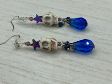 Load image into Gallery viewer, Mini Howlite Skull Bead Earrings large star shaped rainbow hematite bead with a large bright blue teardrop shaped glass bead on the bottom of the skull for max shimmer and movement. Ultimate Chingona, Cabrona, Latina Chicana, Goth, Vampire Goth, Dark Witchy, La Bruja Style. You can dress these up or down, it will definitely give your outfit a unique look. You can dress these up or down, it will definitely give your outfit a unique look. Measurements: 2 ” in length