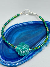 Load image into Gallery viewer, This blue-green pressed glass floral beaded bracelet is a nature-inspired accessory that adds a hint of summer to any look. Crafted with intricate green-blue pressed glass beads and metal wire, the bracelet has an iridescent shimmer finish and a lobster claw clasp for secure wear. Perfect for day-to-night looks. Measurements:  Bracelet: 8 1/2" in length   Earrings: 1 1/4" length