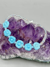 Load image into Gallery viewer, Light blue pressed glass bracelet featuring floral beading is detailed with an iridescent shimmer finish. The bracelet is crafted with metal wire and a lobster claw clasp for easy and secure fastening. Measurements: Bracelet: 8 1/4" in length