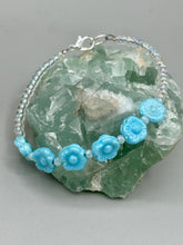 Load image into Gallery viewer, Light blue pressed glass bracelet featuring floral beading is detailed with an iridescent shimmer finish. The bracelet is crafted with metal wire and a lobster claw clasp for easy and secure fastening. Measurements: Bracelet: 8 1/4" in length