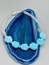 Load image into Gallery viewer, Light blue pressed glass bracelet featuring floral beading is detailed with an iridescent shimmer finish. The bracelet is crafted with metal wire and a lobster claw clasp for easy and secure fastening. Measurements: Bracelet: 8 1/4" in length