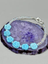 Load image into Gallery viewer, Light blue pressed glass bracelet featuring floral beading is detailed with an iridescent shimmer finish. The bracelet is crafted with metal wire and a lobster claw clasp for easy and secure fastening. Measurements: Bracelet: 8 1/4" in length