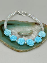 Load image into Gallery viewer, Light blue pressed glass bracelet featuring floral beading is detailed with an iridescent shimmer finish. The bracelet is crafted with metal wire and a lobster claw clasp for easy and secure fastening. Measurements: Bracelet: 8 1/4" in length
