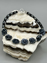 Load image into Gallery viewer, This black metallic floral glass bead and hematite cylinder shaped bracelet is a highly versatile piece; its sleek style can be dressed up or down to match any ensemble. It is constructed of metal wire and features a lobster claw clasp for closing.  Measurements:  Bracelet: 8 1/2" in length
