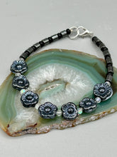Load image into Gallery viewer, This black metallic floral glass bead and hematite cylinder shaped bracelet is a highly versatile piece; its sleek style can be dressed up or down to match any ensemble. It is constructed of metal wire and features a lobster claw clasp for closing.  Measurements:  Bracelet: 8 1/2" in length