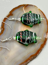 Load image into Gallery viewer, These nature-inspired glass fish earrings are the perfect addition to your boho look. Featuring a delightful dark green hue, the large puffy fish will bring a hippie vibe to your style. Measurements: 1 1/2” in length