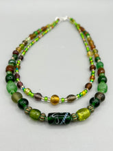 Load image into Gallery viewer, Two strands of beads compose this necklace, featuring a striking combination of light and dark greens, amber, golds, and dark browns. A mixture of glass and metal beads with patina color adds texture and beauty to this unique, bold statement piece. Measurements: Necklace is 17 1/2” in length, can be adjusted up to 19"