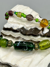 Load image into Gallery viewer, Two strands of beads compose this necklace, featuring a striking combination of light and dark greens, amber, golds, and dark browns. A mixture of glass and metal beads with patina color adds texture and beauty to this unique, bold statement piece. Measurements: Necklace is 17 1/2” in length, can be adjusted up to 19"