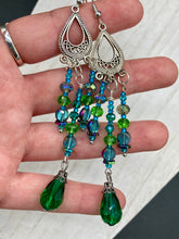 Load image into Gallery viewer, This Whimsical Blue Green Peacock Inspired Beaded Earrings set features bold chandelier style earrings with three long strands of glass bead. These show-stopping pieces boast a range of shimmering shades of blue, green, purple, and gold. A perfect addition to any fashionista's collection. Measurements: 3 1/2” in length