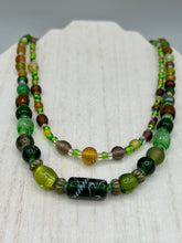 Load image into Gallery viewer, Two strands of beads compose this necklace, featuring a striking combination of light and dark greens, amber, golds, and dark browns. A mixture of glass and metal beads with patina color adds texture and beauty to this unique, bold statement piece. Measurements: Necklace is 17 1/2” in length, can be adjusted up to 19"