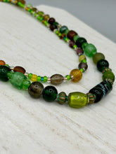 Load image into Gallery viewer, Two strands of beads compose this necklace, featuring a striking combination of light and dark greens, amber, golds, and dark browns. A mixture of glass and metal beads with patina color adds texture and beauty to this unique, bold statement piece. Measurements: Necklace is 17 1/2” in length, can be adjusted up to 19"
