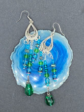 Load image into Gallery viewer, This Whimsical Blue Green Peacock Inspired Beaded Earrings set features bold chandelier style earrings with three long strands of glass bead. These show-stopping pieces boast a range of shimmering shades of blue, green, purple, and gold. A perfect addition to any fashionista's collection. Measurements: 3 1/2” in length