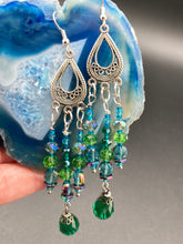 Load image into Gallery viewer, This Whimsical Blue Green Peacock Inspired Beaded Earrings set features bold chandelier style earrings with three long strands of glass bead. These show-stopping pieces boast a range of shimmering shades of blue, green, purple, and gold. A perfect addition to any fashionista's collection. Measurements: 3 1/2” in length