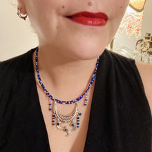 Load image into Gallery viewer, This stylish choker necklace showcases a large half moon pendant, adorned with glass beads and small, dangling crescent moon charms. Its eye-catching hues, of blue and silver, are complemented with delicate tints of purple and pink. Boasting an accentuated look and ample motion, this piece is sure to impress. Measurements: Necklace is 16 1/2”adjustable up to 18"