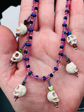 Load image into Gallery viewer, Dark gothic, elegant, and romantic necklace contains two beaded strands of pink beads that contain a dash of purple, blue, and gold hues. Tiny skull howlite skulls with rainbow hematite heart shaped beads to give this necklace a cute and romantic style. Comes with matching earrings. Necklace is 14”adjustable up to 18" in length - hanging skulls and hearts pendant are 1”