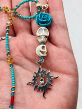 Load image into Gallery viewer, Enchanting Southwest Style Jewelry. Necklace captures Frida Kahlo's signature floral crown on her head. Howlite skull beads topped with turquoise quartize floral beads, style to represent mother and child. Dangling shimmery sun charm pendant to incorporated some movement. Chingona, Cabrona, Latina Chicana, Goth, Vampire Goth, Dark Witchy Style. This piece of jewelry can be worn for inspiration or a great Dia De Los Muertos jewelry piece. Necklace is 20” in length - flower, skull, and sun pendant is 3”