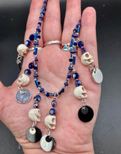 Load image into Gallery viewer, Stunning Cascade of Edgy Gun Metal Shimmery Glass Bead Necklace. Contains six dangling strands of beautiful and bold skulls and glass beads. A variety of shapes and different color glass beads are used that contain hues of silver, purple, pink, blue, and gold tones. This bold and beautiful necklace comes with dainty matching earrings to complete the look. Measurements: Necklace is 14 1/2” adjustable up to 18" - each glass skulls measures 1 3/4” in Height