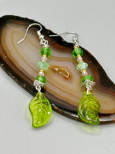 Load image into Gallery viewer, Long strand of glittering light green and gold glass beads, as well as a leaf-shaped glass charm at the bottom, combine to create a highly dynamic effect. These versatile earrings, perfect for a whimsical fairy princess, good witch, or nature-loving hippie look, draw on nature-inspired designs, providing the ideal finishing touch to any ensemble. Measurements: 2 1/4” in length