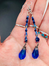 Load image into Gallery viewer, This stunning, one of a kind pair of celestial beaded earrings is a bold addition to any jewelry collection. Crafted with vibrant blue glass beads, the color contains varied shades of blue, purple, and hints of gold to create unique texture. The design is inspired by the awe-inspiring beauty of the majestic galaxy. Measurements: 2 3/4 ” in length