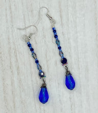 Load image into Gallery viewer, This stunning, one of a kind pair of celestial beaded earrings is a bold addition to any jewelry collection. Crafted with vibrant blue glass beads, the color contains varied shades of blue, purple, and hints of gold to create unique texture. The design is inspired by the awe-inspiring beauty of the majestic galaxy. Measurements: 2 3/4 ” in length
