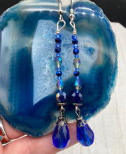 Load image into Gallery viewer, This stunning, one of a kind pair of celestial beaded earrings is a bold addition to any jewelry collection. Crafted with vibrant blue glass beads, the color contains varied shades of blue, purple, and hints of gold to create unique texture. The design is inspired by the awe-inspiring beauty of the majestic galaxy. Measurements: 2 3/4 ” in length