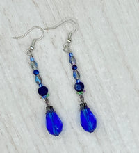 Load image into Gallery viewer, This stunning, one of a kind pair of celestial beaded earrings is a bold addition to any jewelry collection. Crafted with vibrant blue glass beads, the color contains varied shades of blue, purple, and hints of gold to create unique texture. The design is inspired by the awe-inspiring beauty of the majestic galaxy. Measurements: 2” in length