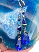 Load image into Gallery viewer, This stunning, one of a kind pair of celestial beaded earrings is a bold addition to any jewelry collection. Crafted with vibrant blue glass beads, the color contains varied shades of blue, purple, and hints of gold to create unique texture. The design is inspired by the awe-inspiring beauty of the majestic galaxy. Measurements: 2” in length