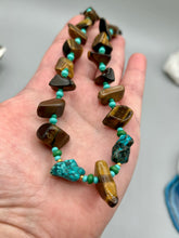 Load image into Gallery viewer, Bold earthy tone necklace contains large natural tigers eye stone chips with blue and green turquoise glass beads. Colorful and bold strand will make a perfect statement piece. Measurements: Necklace is 18 3/4 " in length adjustable to 20"This bold earthy tone necklace presents an eye-catching combination of natural tigers eye stone chips and blue-green turquoise glass beads, making it an ideal statement piece. Measurements: Necklace is 18 3/4 " in length adjustable to 20"