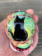 Load image into Gallery viewer, Inspired by nature, ceramic skull is full of vibrant colors and intricate details. The primary color is white with a black cat silhouette and multi-color floral motifs, along with hearts and leaves and lively colorful accents around the entire skull. Mini skull represented the eternal love for a special kitty cat in your life. Black cat silhouette is sitting on a tree branch admiring the starry night sky. Art created for all the cat lovers who adore their sweet kitty. Measurements: H 2 3/4” x W 2” x D 2”
