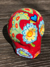 Load image into Gallery viewer, This hand-painted Mini Dia de Los Muertos ceramic skull art provides a vibrant representation of summertime blooms. Its fire red and nature-inspired design is unique, capturing the energy and beauty of a hot day at Meadowlark Gardens in Virginia. A perfect addition to any art collection. Measurements: H 2 3/4” x W 2” x D 2”