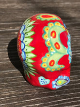 Load image into Gallery viewer, This hand-painted Mini Dia de Los Muertos ceramic skull art provides a vibrant representation of summertime blooms. Its fire red and nature-inspired design is unique, capturing the energy and beauty of a hot day at Meadowlark Gardens in Virginia. A perfect addition to any art collection. Measurements: H 2 3/4” x W 2” x D 2”