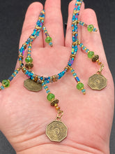 Load image into Gallery viewer, This collar-style necklace is a showstopper, beaded with stylish glass beads in green and blue tones, featuring contrasting yin-yang charms with differing sides. Rectangular rainbow hematite beads add complexity and depth, and double-hole matte gold beads keep the collar shape complete. It gracefully drapes around the neck, making a timeless statement of elegance.  Measurements:  Necklace is 14”, can be adjusted up to 18"