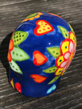 Load image into Gallery viewer, Inspired by nature, this ceramic skull statuette is full of vibrant color and intricate details. The primary color is royal blue with multi-color floral motifs that are painted across the skull, along with hearts and leaves and lively colorful accents around the entire skull.