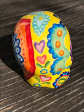 Load image into Gallery viewer, Inspired by nature, this ceramic skull statuette is full of vibrant color and intricate details. The primary color is yellow with Multi-color floral motifs that are painted across the skull, along with hearts and leaves and lively colorful accents around the entire skull.