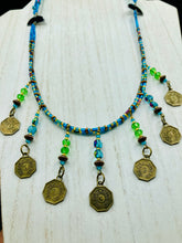 Load image into Gallery viewer, This necklace features vivid green and blue glass beading and a yin yang brass octagon charm. Each side of the charm is distinct, creating a two-in-one look. The look is further enhanced with the addition of rectangular rainbow hematite beads for added visual complexity. Double-hole flat matte gold beads keep the collar shape and add to the necklace's elegant draping when worn.  Measurements:    Necklace is 23” in length