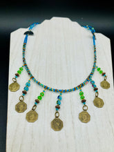 Load image into Gallery viewer, This necklace features vivid green and blue glass beading and a yin yang brass octagon charm. Each side of the charm is distinct, creating a two-in-one look. The look is further enhanced with the addition of rectangular rainbow hematite beads for added visual complexity. Double-hole flat matte gold beads keep the collar shape and add to the necklace's elegant draping when worn.  Measurements:    Necklace is 23” in length
