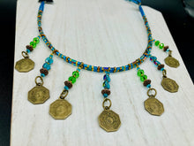 Load image into Gallery viewer, This necklace features vivid green and blue glass beading and a yin yang brass octagon charm. Each side of the charm is distinct, creating a two-in-one look. The look is further enhanced with the addition of rectangular rainbow hematite beads for added visual complexity. Double-hole flat matte gold beads keep the collar shape and add to the necklace's elegant draping when worn.  Measurements:    Necklace is 23” in length