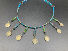 Load image into Gallery viewer, This necklace features vivid green and blue glass beading and a yin yang brass octagon charm. Each side of the charm is distinct, creating a two-in-one look. The look is further enhanced with the addition of rectangular rainbow hematite beads for added visual complexity. Double-hole flat matte gold beads keep the collar shape and add to the necklace's elegant draping when worn.  Measurements:    Necklace is 23” in length