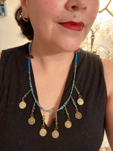 Load image into Gallery viewer, This necklace features vivid green and blue glass beading and a yin yang brass octagon charm. Each side of the charm is distinct, creating a two-in-one look. The look is further enhanced with the addition of rectangular rainbow hematite beads for added visual complexity. Double-hole flat matte gold beads keep the collar shape and add to the necklace's elegant draping when worn.  Measurements:    Necklace is 23” in length