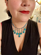 Load image into Gallery viewer, This necklace features vibrant teal quartzite and glass beads. The quartzite beads have a captivating swirl pattern, combining dark red and dark blue hues. It has an ethereal feel thanks to the various shades of blues, golds, and greens used to create a two-strand beaded design. For a dramatic finish, seven strands are added, completed with rectangular rainbow hematite beads for texture and depth. Both strands are held together with double-hole flat matte gold beads to keep a collar shape.