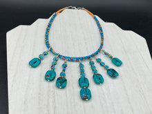 Load image into Gallery viewer, This necklace features vibrant teal quartzite and glass beads. The quartzite beads have a captivating swirl pattern, combining dark red and dark blue hues. It has an ethereal feel thanks to the various shades of blues, golds, and greens used to create a two-strand beaded design. For a dramatic finish, seven strands are added, completed with rectangular rainbow hematite beads for texture and depth. Both strands are held together with double-hole flat matte gold beads to keep a collar shape.