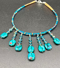 Load image into Gallery viewer, This necklace features vibrant teal quartzite and glass beads. The quartzite beads have a captivating swirl pattern, combining dark red and dark blue hues. It has an ethereal feel thanks to the various shades of blues, golds, and greens used to create a two-strand beaded design. For a dramatic finish, seven strands are added, completed with rectangular rainbow hematite beads for texture and depth. Both strands are held together with double-hole flat matte gold beads to keep a collar shape.