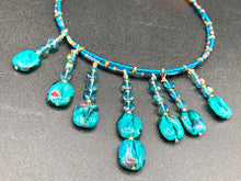 Load image into Gallery viewer, This necklace features vibrant teal quartzite and glass beads. The quartzite beads have a captivating swirl pattern, combining dark red and dark blue hues. It has an ethereal feel thanks to the various shades of blues, golds, and greens used to create a two-strand beaded design. For a dramatic finish, seven strands are added, completed with rectangular rainbow hematite beads for texture and depth. Both strands are held together with double-hole flat matte gold beads to keep a collar shape.