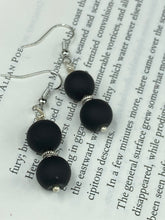 Load image into Gallery viewer, These flat matte black glass bead earrings are perfect for creating a cocktail chic ensemble. With a round shape and silver plated floral bead, this timeless piece is ideal for special occasions such as weddings. Its minimalist look exudes effortless elegance. Measurements: 1 1/4” in length