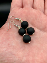 Load image into Gallery viewer, These flat matte black glass bead earrings are perfect for creating a cocktail chic ensemble. With a round shape and silver plated floral bead, this timeless piece is ideal for special occasions such as weddings. Its minimalist look exudes effortless elegance. Measurements: 1 1/4” in length