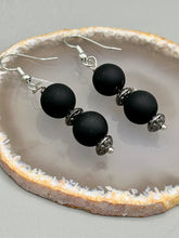 Load image into Gallery viewer, These flat matte black round glass bead earrings with silver plated floral beads offer a versatile look perfect for cocktail chic attire, a wedding necklace, and minimalist style. Measurements: 1 1/4” in length