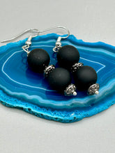 Load image into Gallery viewer, These flat matte black round glass bead earrings with silver plated floral beads offer a versatile look perfect for cocktail chic attire, a wedding necklace, and minimalist style. Measurements: 1 1/4” in length