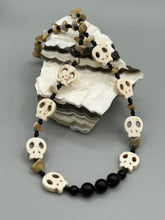 Load image into Gallery viewer, This skully necklace is full of neutral tones and is adorned with natural black obsidian and bamboo chips, as well as small glass beads. It has a unique design that creates a striking silhouette across the wearer's neck. An ideal statement piece for bold fashion enthusiasts. Measurements: Necklace - 19 1/4"