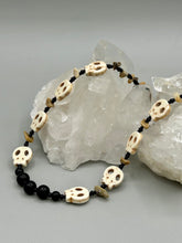 Load image into Gallery viewer, This skully necklace is full of neutral tones and is adorned with natural black obsidian and bamboo chips, as well as small glass beads. It has a unique design that creates a striking silhouette across the wearer's neck. An ideal statement piece for bold fashion enthusiasts. Measurements: Necklace - 19 1/4"